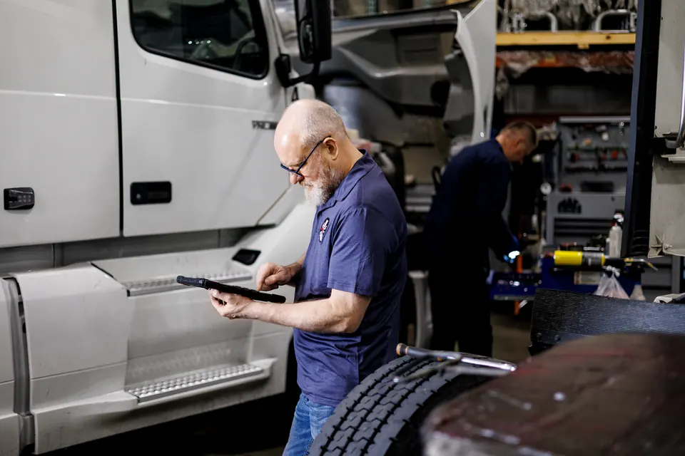 Two technicians with a clipboard inspecting underneath a white truck at Truck Clinic in Romeoville